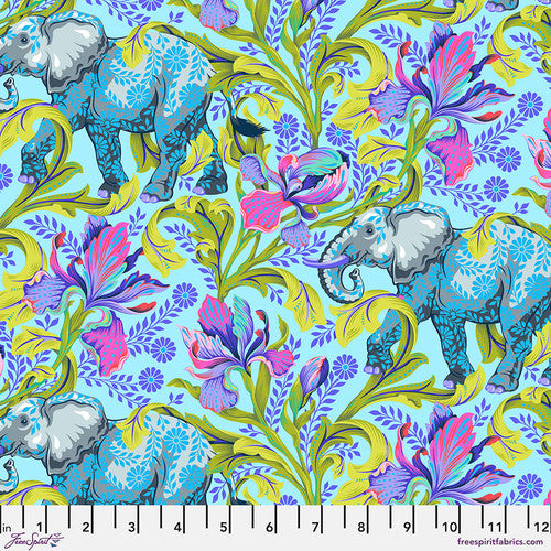 A bright and wild floral print done in different purples and greens with elephants intermixed throughout. Secondary floral patterns of purple and blue are layered on top. Background is a Sky Blue. Fabric