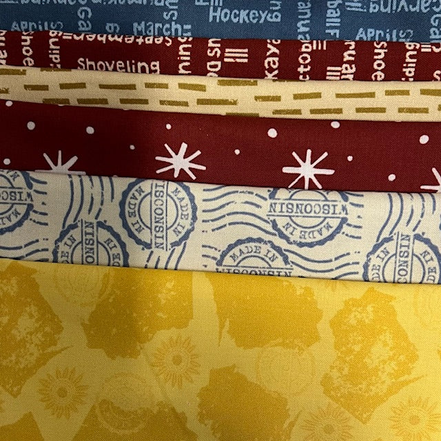 Stack of fabric half-yards with various patterns including text, stamps, and floral designs.